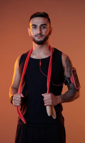 Handsome serious sportsman in headphones and armband holding jumping rope while looking at camera